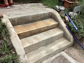 A set of concrete steps leading up to a porch, which are in need of some improvement.