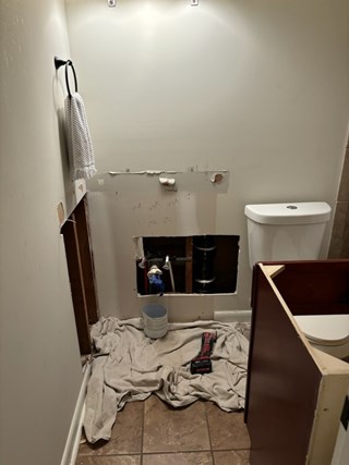A bathroom wall with part of the drywall removed, exposing plumbing and a work-in-progress area.
