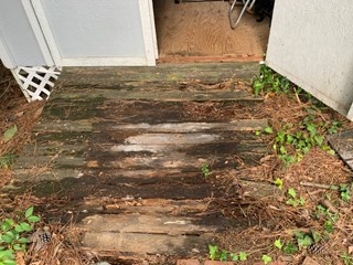 Wooden ramp leading to a shed that is worn out, with noticeable wood rot and deterioration.