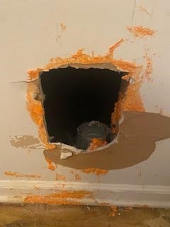 A large hole in the drywall near the floor where the dryer vent exits.  