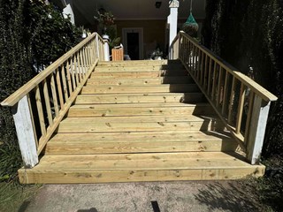Porch stairs repaired with new untreated wood. The steps are sturdy and level, with fresh planks replacing the damaged ones. The railing has been replaced and is now intact.