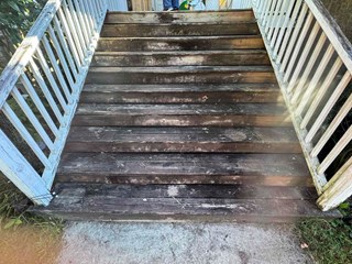 A set of wooden stairs leading to a porch, with significant wear on the steps.