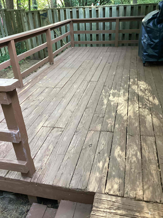 A deck with wooden flooring that shows signs of wear and aging. The boards are visibly weathered and some sections are slightly damaged or warped. 