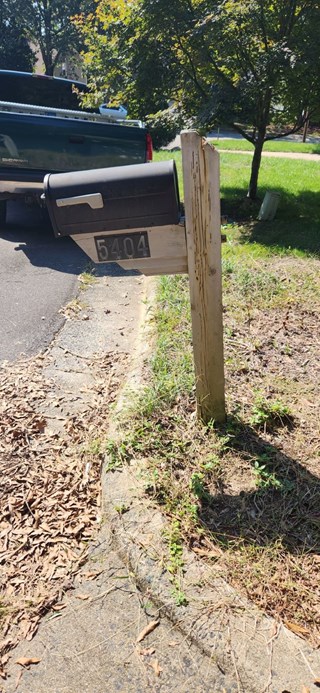Mailbox mounted on a weathered wooden post, with visible damage to the structure. 