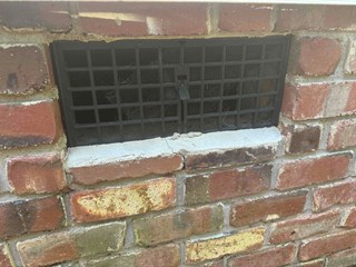 A crawlspace vent on the side of a house with visible damage.