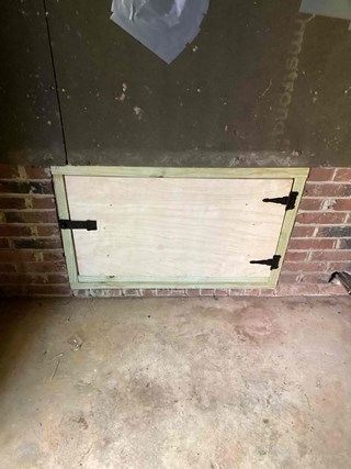 Crawlspace entry is now securely covered with a newly installed wooden door.