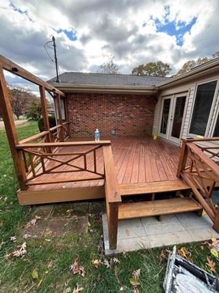 A deck area with wooden flooring and a set of steps leading down to the ground. The deck has some visible wear, including faded wood and weathered railings.