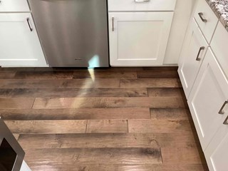 Kitchen floor after the repair. The damaged, discolored floorboards have been replaced with new, intact hardwood flooring. 