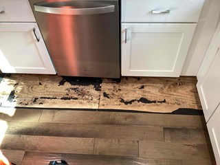 A section of kitchen flooring with visible water damage around the area of the dishwasher. 