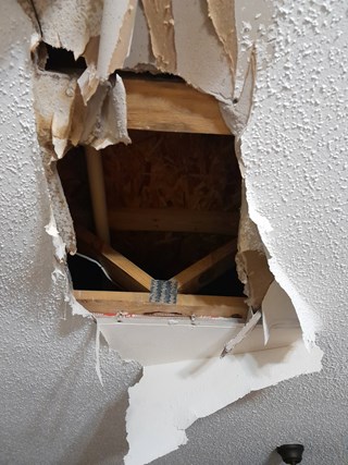 A hole in the ceiling drywall, with the damaged area exposing the wooden beams and insulation behind it.