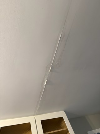Ceiling with visible damage, showing a long crack in the drywall, due to water damage. 