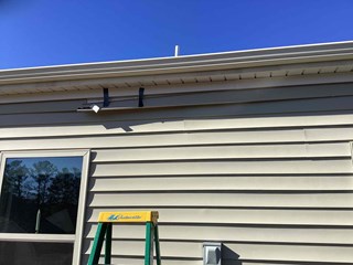 Durham, NC 27703 vinyl siding repair: A professional contractor is repairing a damaged section of siding using temporary straps for support.