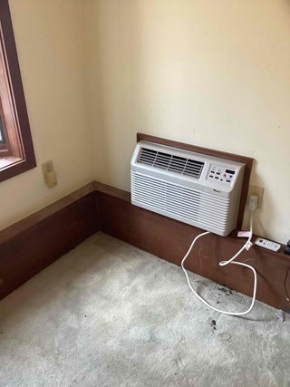 Amana window air conditioning unit mounted in a window frame, providing cooling to a carpeted room.