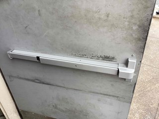 Detail of a code-compliant push bar being installed on a restaurant emergency exit in Cary, NC. Highlights the hardware and the professional installation by Ace Handyman Serices