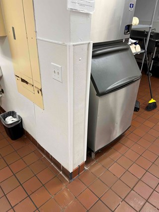 Repaired wall corner in a commercial kitchen, Raleigh, NC 27610. The damaged section has been replaced, and the wall is now smooth and clean. A Manitowoc ice machine is visible on the right.