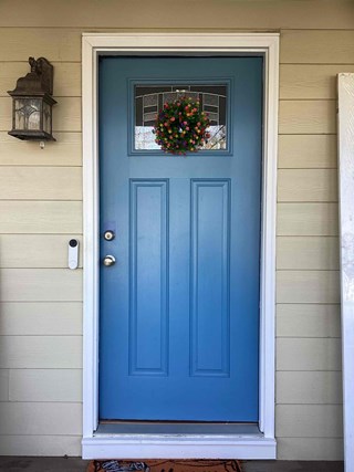  Front entrance in Apex, NC 27502 before handyman storm door installation. Shows the existing blue door with details like the hardware, window, wreath, and surrounding siding.