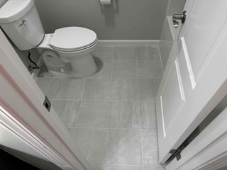 After photo of a remodeled bathroom in Raleigh, NC 27613, featuring new gray tile flooring, a white toilet, and fresh gray paint