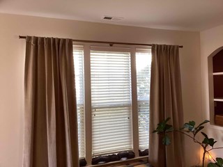  After photo of a window with newly installed, long, tan curtains flanking white faux wood blinds in Raleigh, NC. The curtains are hung on a decorative rod, softening the light and framing the window.