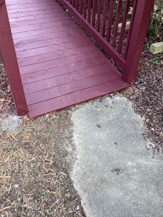 efore photo of a ramp transition in Raleigh, North Carolina, showing a red stained wooden ramp meeting a gray concrete surface.