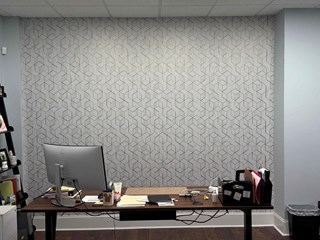 Raleigh 27615 office renovation complete: geometric wallpaper installed. This after photo displays a modern black and white cube design wallpaper, transforming the office space behind a desk and computer monitor.