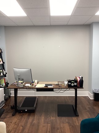 Photo showing a blank office wall in Raleigh, NC 27615, before wallpaper installation. Features a desk with a computer and a treadmill.