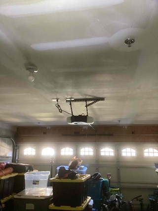 A garage interior after the ceiling repair is complete. The ceiling is now smooth, and a round garage door opener is mounted on it.