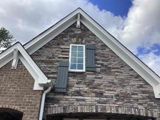 Wake Forest, NC, home before shutter repair: damaged gray shutter on stone and brick facade.