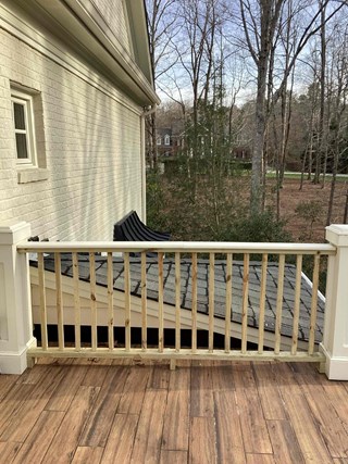After photo showing a newly installed wood railing on a deck. The railing is made of light-colored wood and features a simple, vertical slat design. The deck is made of wood planks with a reddish-brown stain.