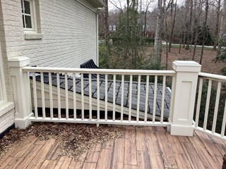This image shows a white wood railing with decorative post caps in 27587, highlighting the need for wood rot repairs. The railing overlooks a wood deck.