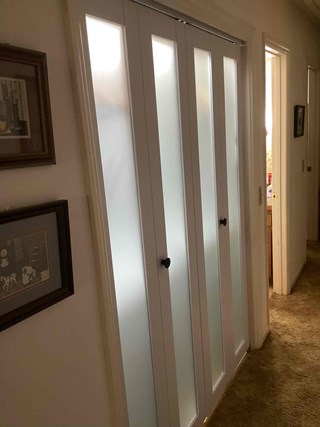 Modern frosted glass wooden bi-fold laundry closet doors installed in hallway of home in Apex, NC 27539 by Ace Handyman Services handyman, enhancing style and concealing storage area.