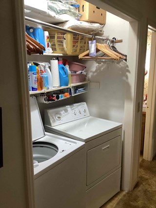 Open laundry closet with washer, dryer, and shelving before frosted glass bi-fold door installation in Apex, NC 27539 by Ace Handyman Services handyman, improving hallway appearance and storage organization.