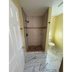 Finished bathroom remodel with tiled walk-in shower, black fixtures, corner shelves, and marble-look floor tile in Raleigh, NC.