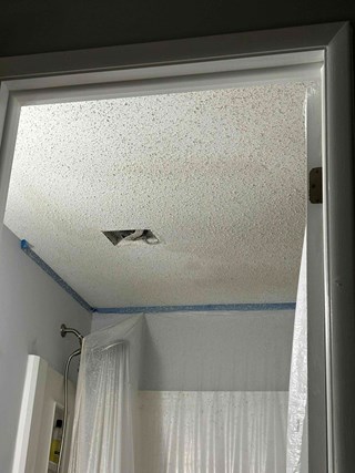 Bathroom ceiling with a textured "popcorn" finish. The area near the ceiling light has a hole due to a water leak.