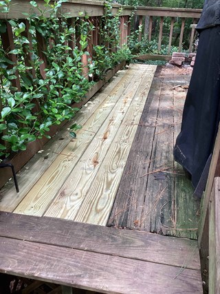 A wooden deck with a mix of old, weathered boards and newly installed, light-colored wood planks. The fresh planks stand out against the darker, worn sections of the deck. 
