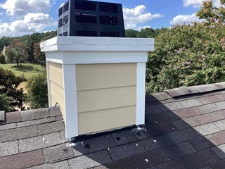 The image shows the chimney after repairs. The exterior trim has been replaced and freshly painted white, giving it a clean and finished appearance. The beige siding remains the same but now has a smooth and polished look. The top trim has also been repainted, and the overall structure looks well-maintained. 