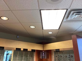 The image shows the same ceiling after repairs. The missing ceiling tiles have been replaced, creating a clean and uniform appearance. The lighting fixtures, including recessed lights and a fluorescent panel, remain unchanged. 