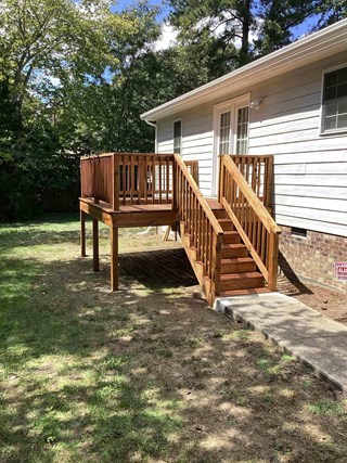 The image shows the same deck after staining. The wood now has a rich, warm color, giving it a finished and polished appearance. The protective coverings on the house have been removed, revealing clean siding and newly painted doors. 