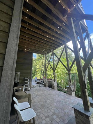 The second image shows the same patio after the installation of Edison-style string lights. The lights are evenly spaced along the underside of the deck, creating a warm and inviting ambiance. Additionally, two hanging hammock chairs have been added, enhancing the cozy and functional atmosphere of the space. 