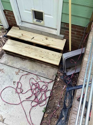 Steps after being rebuilt with fresh, light-colored wooden planks. The new steps look sturdy and clean, providing an improved entrance to the door. 