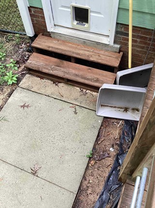 Old wooden steps leading to a white door with a pet door installed at the bottom. The steps are weathered and darkened from exposure, with visible wear and dirt.