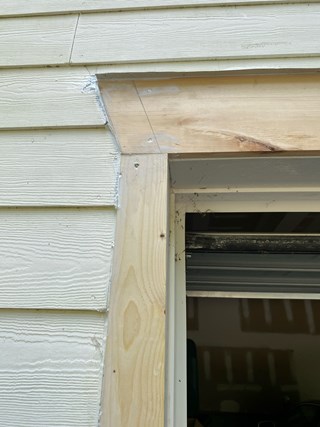 The rotted wood has been replaced with fresh, untreated wooden trim, and gaps have been sealed with caulking. The new wood appears clean and sturdy, contrasting with the existing siding, which remains unpainted.
