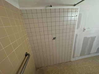 Commercial shower wall after restoration, now fully covered with clean, neatly arranged white tiles.