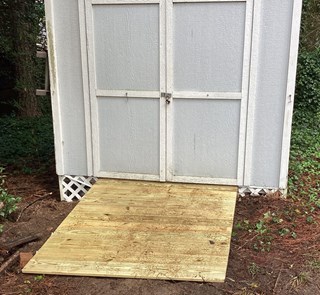 A small wooden shed with a freshly built ramp in front. The ramp is sturdy and smooth, made of clean, unweathered wood with evenly spaced planks.