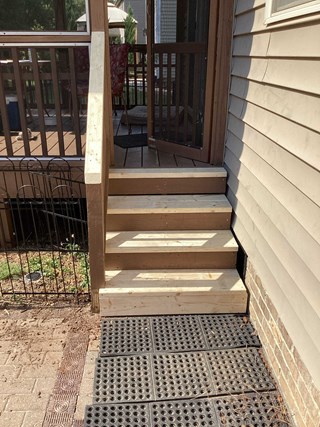 A newly rebuilt set of wooden deck steps leading up to a screened porch. 