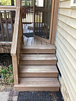 Weathered wooden deck steps showing signs of aging, discoloration, and wear. The wood appears faded, with visible cracks and rough textures. 