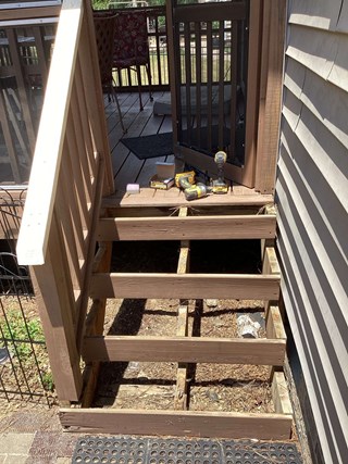  A partially dismantled set of wooden deck steps leading up to a screened porch. The steps have been removed, exposing the wooden frame and support structure beneath.