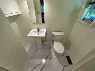 A newly renovated bathroom featuring a pedestal sink and a modern toilet. The floor is updated with sleek white tiles accented by subtle gray veining. The clean and minimalist design gives the space a refreshed and contemporary appearance.