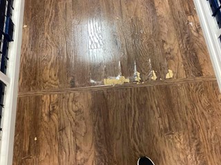 Damaged wooden floor with noticeable peeling, chipping, and scratches.