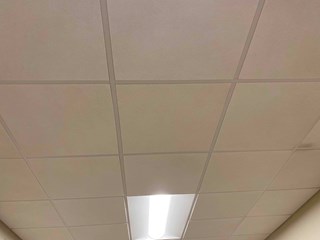 Drop ceiling after the damaged tile has been replaced. The ceiling tiles are now uniform in color and free of any visible stains or damage.