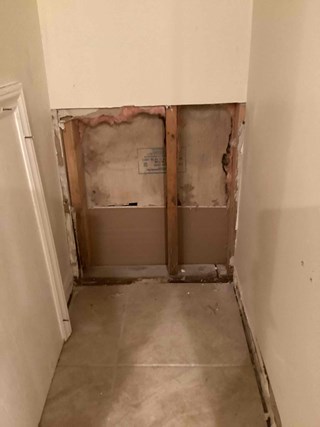 A closet corner with a large section of missing drywall exposing wooden studs and insulation.